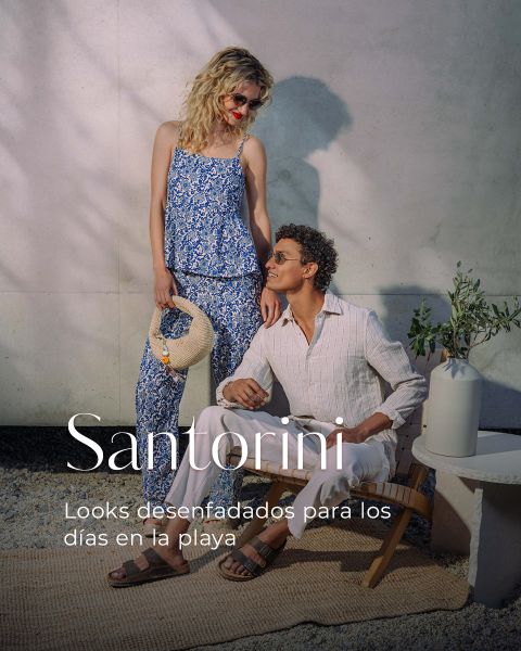 Una mujer con un atuendo estampado azul está de pie junto a un hombre sentado con ropa clara. El texto dice: "Santorini. Looks desenfadados para los días en la playa.".