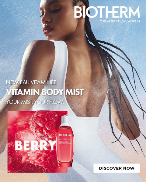 Una mujer vestida de blanco está de espaldas a la cámara en la niebla. Se ve una botella de «Biotherm Vitamin Body Mist»; el texto promociona la fragancia «Pulsation Berry».