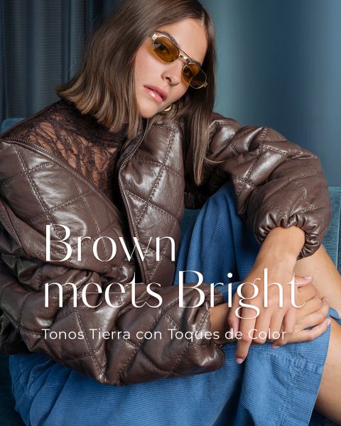 Una mujer con una chaqueta acolchada marrón, unos pantalones azules y unas gafas de sol amarillas está sentada, con el brazo apoyado sobre la rodilla. Texto: «El marrón se encuentra con lo vibrante. Tonos tierra con toques de color.».