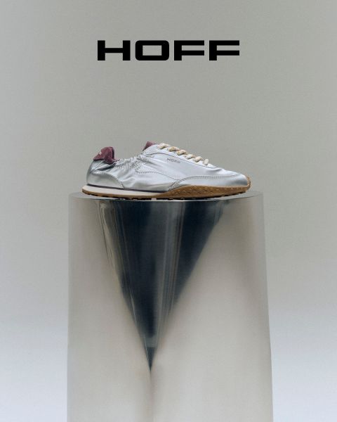 Una zapatilla plateada con tacón morado se apoya sobre un pedestal reflectante bajo el logo "HOFF" sobre un fondo gris claro.