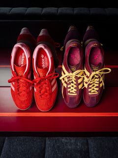 Dos pares de zapatillas adidas: uno rojo con rayas blancas, el otro morado con rayas amarillas, uno al lado del otro sobre una superficie a rayas rojas.