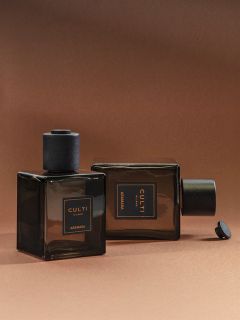 Dos frascos de perfume cuadrados de cristal oscuro con la inscripción «CULTI MILANO ARAMARA» sobre un fondo marrón; uno está de pie, el otro está tumbado de lado.