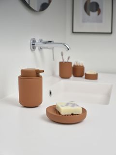 Un lavabo moderno con dispensador de jabón marrón, jabonera y accesorios sobre una encimera blanca, así como un grifo de pared instalado encima.