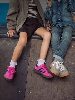 Dos niños están sentados uno al lado del otro en una rampa; solo se ven sus piernas y zapatillas - uno lleva zapatillas rosas, el otro zapatillas grises y vaqueros.