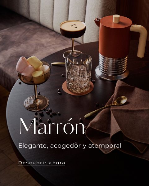 Una mesa redonda con bebidas de café, malvaviscos, una cafetera, un vaso, una servilleta marrón y cubiertos dorados en un ambiente acogedor. Sobre la imagen se muestra un texto en español.