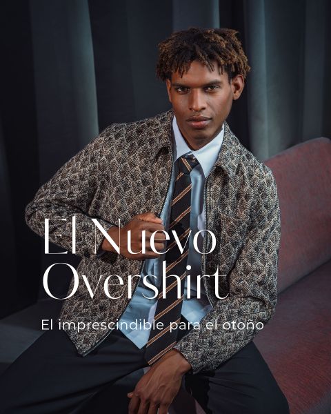 Un hombre con una sobrecamisa estampada, una camisa azul claro y una corbata a rayas está sentado en un sofá. Texto: «El Nuevo Overshirt. Un imprescindible para el otoño.»