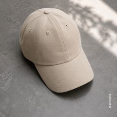 Sobre un suelo de baldosas grises yace una gorra de béisbol beige, en el fondo se aprecian la luz del sol y sombras suaves.