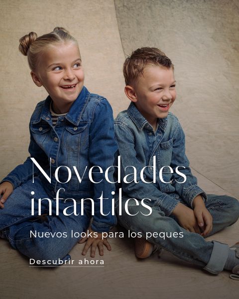 Dos niños pequeños con conjuntos vaqueros están sentados en un skatepark y sonríen. Un texto en español promociona nuevos looks para niños e invita a descubrir.