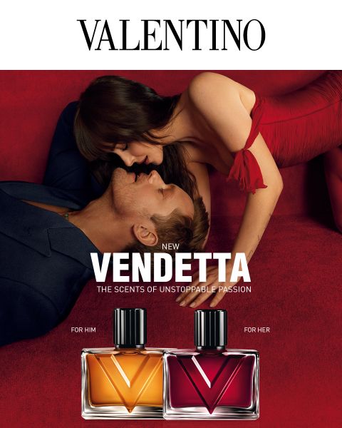 Un hombre y una mujer con ropa elegante se abrazan sobre terciopelo rojo junto a los frascos de perfume "Valentino Vendetta", uno etiquetado como "For Him" y el otro como "For Her".