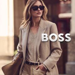 Una mujer con un blazer beige y gafas de sol, llevando un bolso con el logo de BOSS.