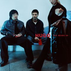 Dos hombres están sentados en un banco, mientras una persona en primer plano sostiene una bolsa de ropa con la inscripción "HUGO RED MEANS GO".