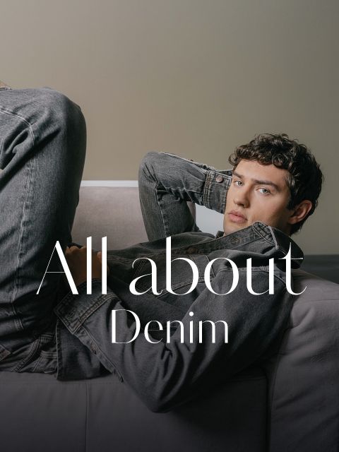 Un joven con una chaqueta vaquera gris y vaqueros está apoyado en un sofá, sobre la imagen se superpone el texto "Todo sobre el denim".