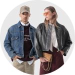 Ein Mann in Jeansjacke und mit einer Mütze steht neben einer Frau in Lederjacke, Sonnenbrille und Rock; beide blicken nach vorne.