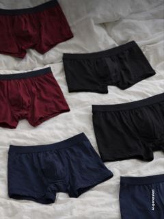 Seis pares de bóxers para hombre en negro, burdeos y azul marino se extienden sobre una base de tela blanca.