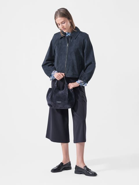 Una mujer con una chaqueta azul marino, culottes y mocasines sostiene un pequeño bolso azul marino y posa frente a un fondo blanco liso.
