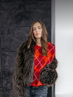 Una mujer lleva un jersey de rombos rojo anaranjado debajo de una chaqueta de piel sintética oscura.