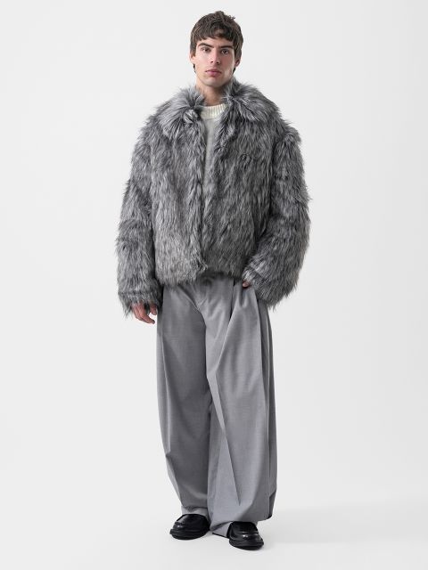 Un hombre que lleva una chaqueta gris de piel sintética, un suéter color crema y pantalones grises de pierna ancha.