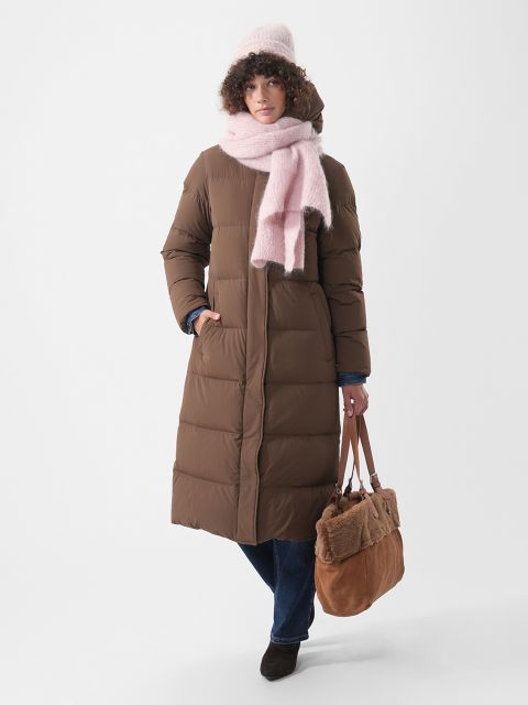 Una persona lleva un abrigo largo de plumas marrón, un gorro rosa y una bufanda rosa, y lleva un bolso tote marrón.