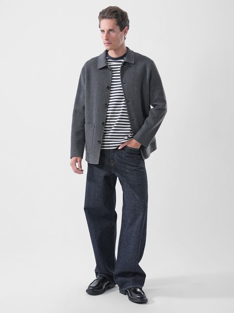Un hombre que lleva una chaqueta gris sobre una camiseta de rayas azul marino y blanco, vaqueros azul oscuro y mocasines negros.